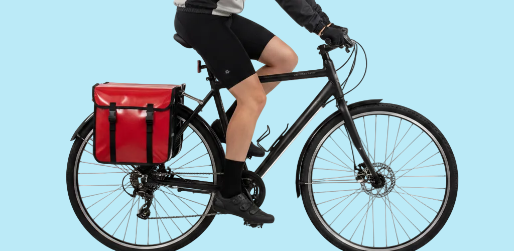 Person riding a bicycle with red panniers against a light blue background